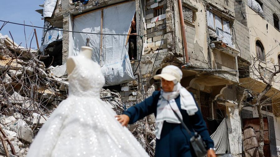 Seorang wanita Palestina melihat gaun pengantin yang dipajang di luar sebuah toko di samping puing-puing dan bangunan yang rusak, karena para pengantin wanita di Gaza beralih ke gaun bekas di tengah kenaikan harga dan kekurangan yang disebabkan oleh perang, di Khan Younis di Jalur Gaza selatan, 9 Mei 2026.