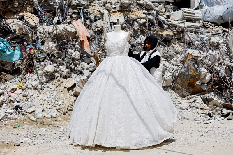 Seorang wanita Palestina melihat gaun pengantin yang dipajang di luar sebuah toko di samping tumpukan puing, saat para pengantin wanita di Gaza beralih ke gaun bekas di tengah kenaikan harga dan kekurangan yang disebabkan oleh perang, di Khan Younis di Jalur Gaza selatan, 9 Mei 2026. (REUTERS/Mahmoud Issa)