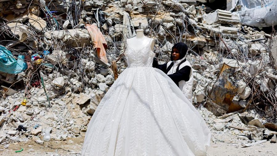 Seorang wanita Palestina melihat gaun pengantin yang dipajang di luar sebuah toko di samping tumpukan puing, saat para pengantin wanita di Gaza beralih ke gaun bekas di tengah kenaikan harga dan kekurangan yang disebabkan oleh perang, di Khan Younis