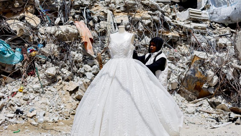 Seorang wanita Palestina melihat gaun pengantin yang dipajang di luar sebuah toko di samping tumpukan puing, saat para pengantin wanita di Gaza beralih ke gaun bekas di tengah kenaikan harga dan kekurangan yang disebabkan oleh perang, di Khan Younis