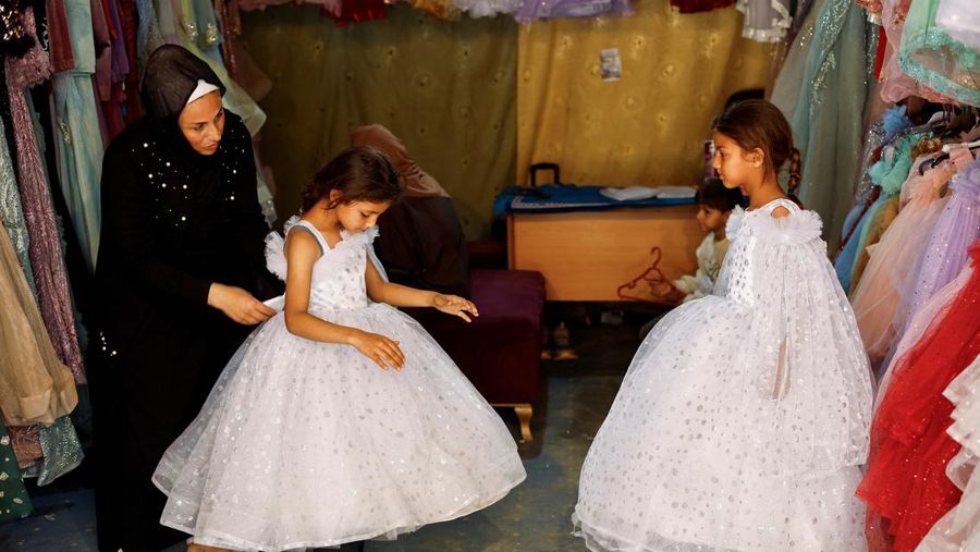 Seorang wanita Palestina membantu dua gadis muda mencoba gaun di sebuah toko, karena para pengantin wanita di Gaza beralih ke gaun bekas di tengah kenaikan harga dan kekurangan yang disebabkan oleh perang, di Khan Younis di Jalur Gaza selatan, 9 Mei 2026.