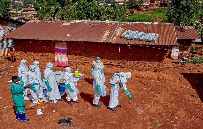 Para pekerja Palang Merah yang mengenakan alat pelindung diri (APD) berjalan dalam formasi saat mereka mendisinfeksi tanah di luar rumah seorang pria tak dikenal yang meninggal karena Ebola, sebelum mengambil jenazahnya, sementara lembaga-lembaga bantuan meningkatkan upaya untuk menahan wabah Ebola baru yang melibatkan strain Bundibugyo, di Quartier Shuni 1, sebuah sektor perumahan di Mongbwalu, Wilayah Djugu, Provinsi Ituri, Republik Demokratik Kongo, 24 Mei 2026. (REUTERS/Gradel Muyisa Mumbere)
