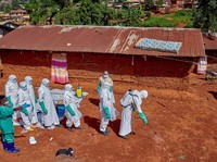 Para pekerja Palang Merah yang mengenakan alat pelindung diri (APD) berjalan dalam formasi saat mereka mendisinfeksi tanah di luar rumah seorang pria tak dikenal yang meninggal karena Ebola, sebelum mengambil jenazahnya, sementara lembaga-lembaga ban