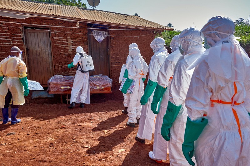 Para pekerja Palang Merah yang mengenakan alat pelindung diri (APD) berjalan dalam formasi saat mereka mendisinfeksi tanah di luar rumah seorang pria tak dikenal yang meninggal karena Ebola, sebelum mengambil jenazahnya, sementara lembaga-lembaga bantuan meningkatkan upaya untuk menahan wabah Ebola baru yang melibatkan strain Bundibugyo, di Quartier Shuni 1, sebuah sektor perumahan di Mongbwalu, Wilayah Djugu, Provinsi Ituri, Republik Demokratik Kongo, 24 Mei 2026. (REUTERS/Gradel Muyisa Mumbere)