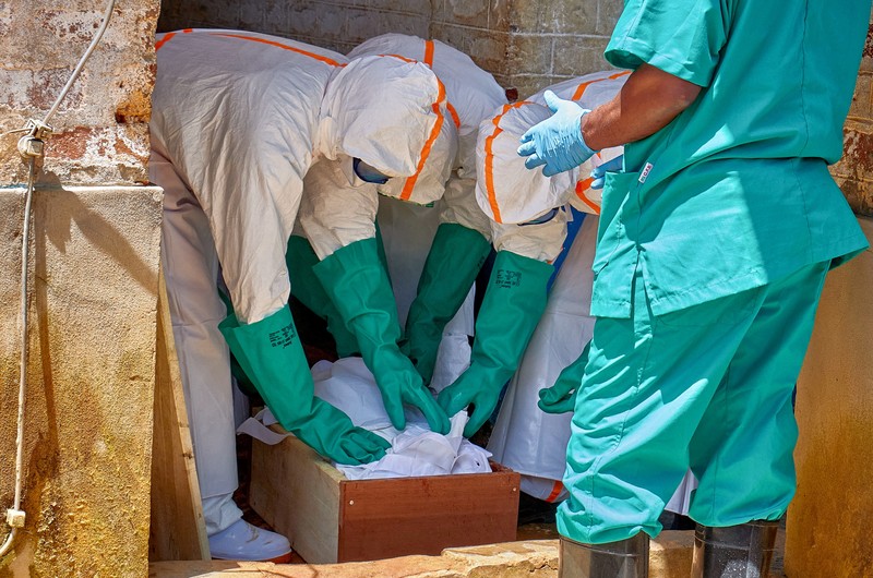 Para pekerja Palang Merah yang mengenakan alat pelindung diri (APD) berjalan dalam formasi saat mereka mendisinfeksi tanah di luar rumah seorang pria tak dikenal yang meninggal karena Ebola, sebelum mengambil jenazahnya, sementara lembaga-lembaga bantuan meningkatkan upaya untuk menahan wabah Ebola baru yang melibatkan strain Bundibugyo, di Quartier Shuni 1, sebuah sektor perumahan di Mongbwalu, Wilayah Djugu, Provinsi Ituri, Republik Demokratik Kongo, 24 Mei 2026. (REUTERS/Gradel Muyisa Mumbere)