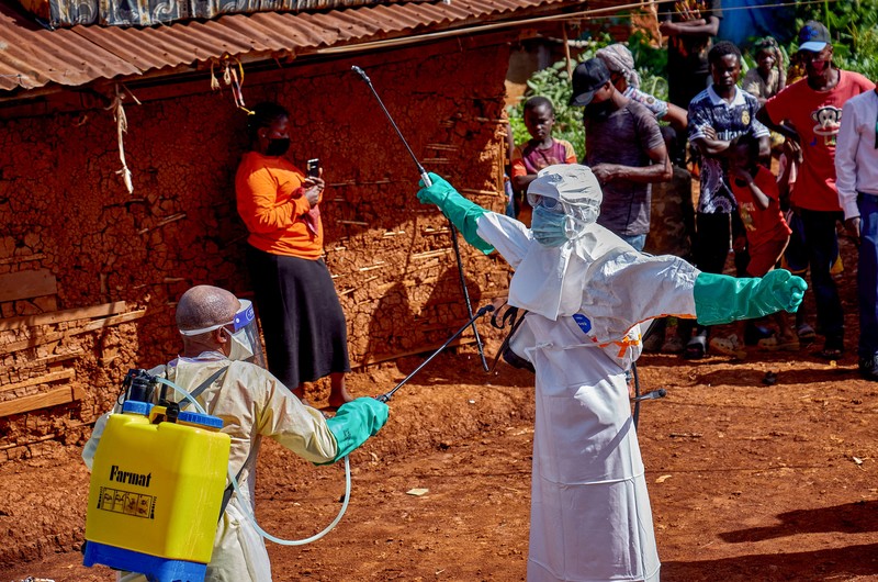 Para pekerja Palang Merah yang mengenakan alat pelindung diri (APD) berjalan dalam formasi saat mereka mendisinfeksi tanah di luar rumah seorang pria tak dikenal yang meninggal karena Ebola, sebelum mengambil jenazahnya, sementara lembaga-lembaga bantuan meningkatkan upaya untuk menahan wabah Ebola baru yang melibatkan strain Bundibugyo, di Quartier Shuni 1, sebuah sektor perumahan di Mongbwalu, Wilayah Djugu, Provinsi Ituri, Republik Demokratik Kongo, 24 Mei 2026. (REUTERS/Gradel Muyisa Mumbere)