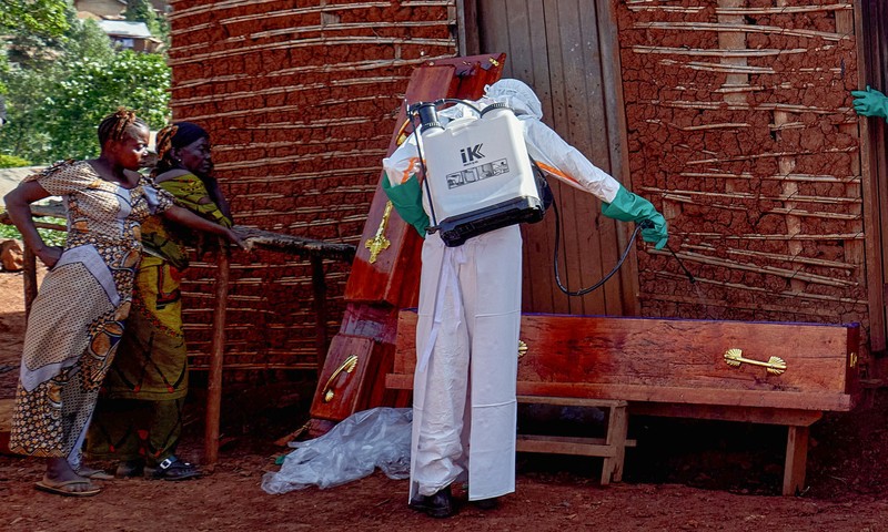 Para pekerja Palang Merah yang mengenakan alat pelindung diri (APD) berjalan dalam formasi saat mereka mendisinfeksi tanah di luar rumah seorang pria tak dikenal yang meninggal karena Ebola, sebelum mengambil jenazahnya, sementara lembaga-lembaga bantuan meningkatkan upaya untuk menahan wabah Ebola baru yang melibatkan strain Bundibugyo, di Quartier Shuni 1, sebuah sektor perumahan di Mongbwalu, Wilayah Djugu, Provinsi Ituri, Republik Demokratik Kongo, 24 Mei 2026. (REUTERS/Gradel Muyisa Mumbere)