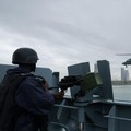 Sebuah helikopter Angkatan Laut Nigeria terbang di dekat NNS Kada, kapal operasional terbesar angkatan laut tersebut, sementara seorang anggota kru memegang senapan mesin selama latihan di luar pelabuhan yang menandai peringatan 70 tahun angkatan lau