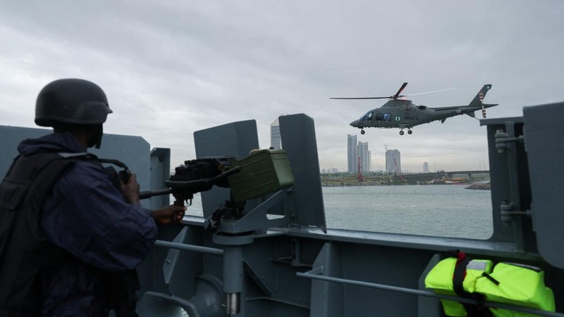 Sebuah helikopter Angkatan Laut Nigeria terbang di dekat NNS Kada, kapal operasional terbesar angkatan laut tersebut, sementara seorang anggota kru memegang senapan mesin selama latihan di luar pelabuhan yang menandai peringatan 70 tahun angkatan laut di sepanjang garis pantai Atlantik di Lagos, Nigeria, 25 Mei 2026.