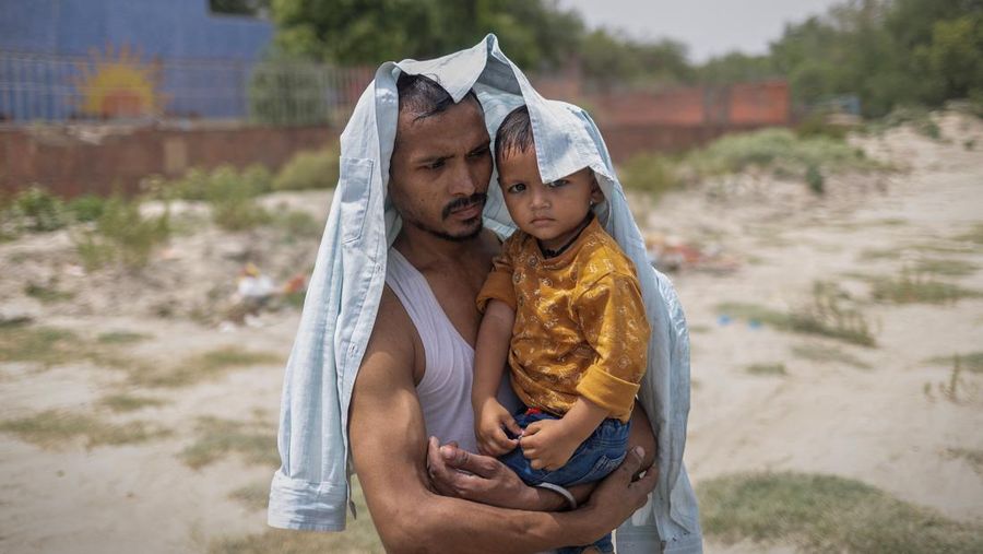 Seorang pria melindungi putranya dari gelombang panas saat ia berdiri di tepi sungai Yamuna pada hari musim panas yang terik di New Delhi, India, 25 Mei 2026.