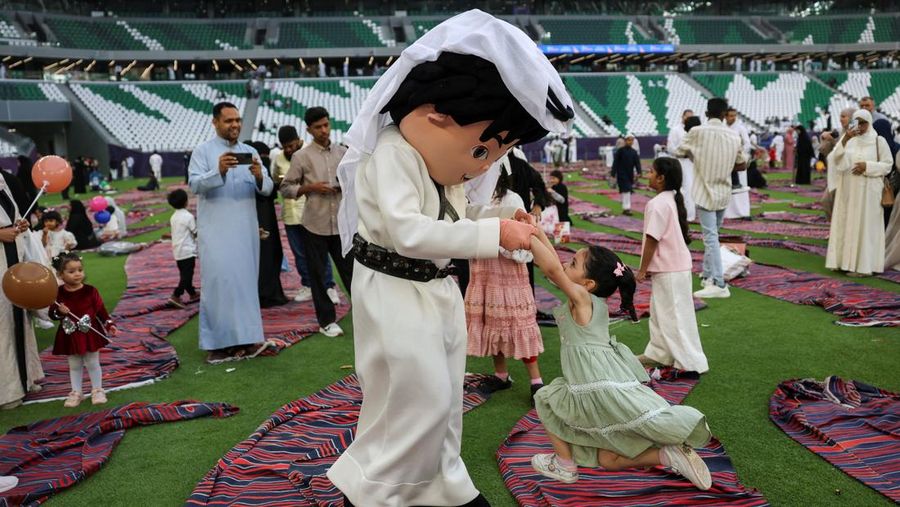 Seseorang yang mengenakan kostum bermain dengan seorang gadis sambil menghibur anak-anak setelah salat Iduladha di Stadion Education City di Al Rayyan, Qatar, Rau (27/5/2026). (REUTERS/Saleh Salem)