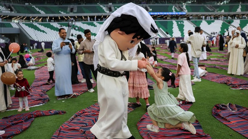 Seseorang yang mengenakan kostum bermain dengan seorang gadis sambil menghibur anak-anak setelah salat Iduladha di Stadion Education City di Al Rayyan, Qatar, Rau (27/5/2026). (REUTERS/Saleh Salem)