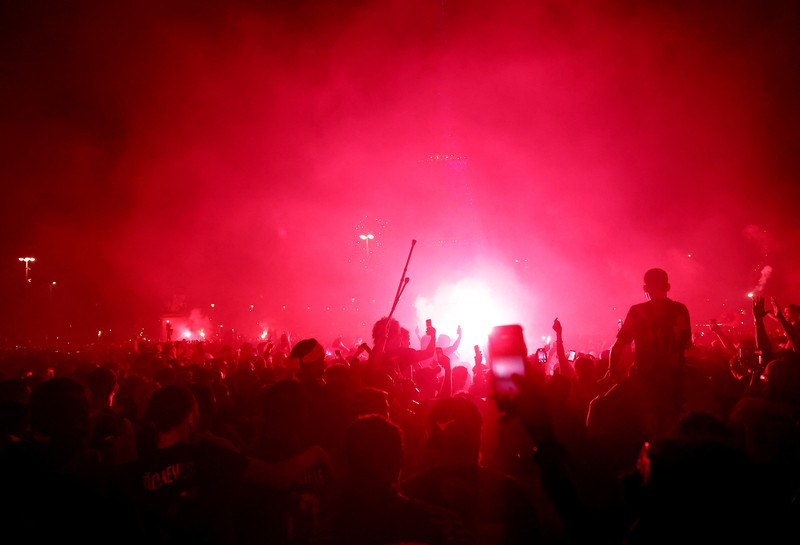 Petugas kepolisian berlindung dari suar yang dinyalakan massa saat perayaan kemenangan Paris Saint-Germain usai menjuarai Liga Champions UEFA di Paris, Minggu (31/5/2026). (REUTERS/Abdul Saboor)