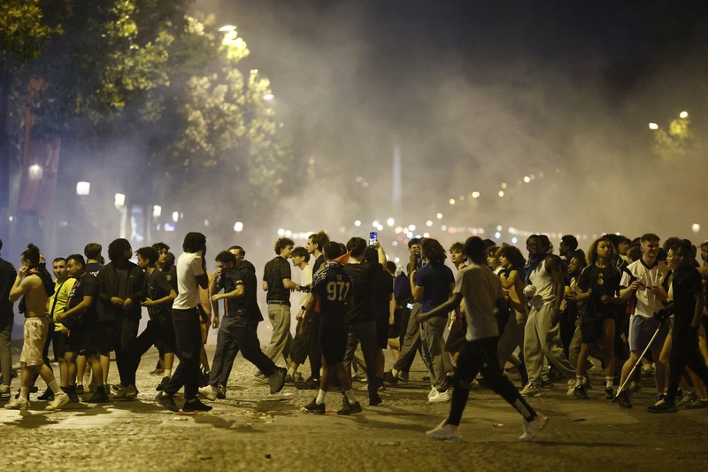 Petugas kepolisian berlindung dari suar yang dinyalakan massa saat perayaan kemenangan Paris Saint-Germain usai menjuarai Liga Champions UEFA di Paris, Minggu (31/5/2026). (REUTERS/Abdul Saboor)