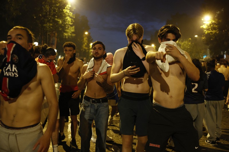 Petugas kepolisian berlindung dari suar yang dinyalakan massa saat perayaan kemenangan Paris Saint-Germain usai menjuarai Liga Champions UEFA di Paris, Minggu (31/5/2026). (REUTERS/Abdul Saboor)
