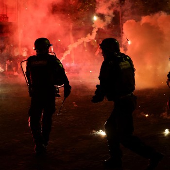 Petugas kepolisian berlindung dari suar yang dinyalakan massa saat perayaan kemenangan Paris Saint-Germain usai menjuarai Liga Champions UEFA di Paris, Minggu (31/5/2026). (REUTERS/Abdul Saboor)
