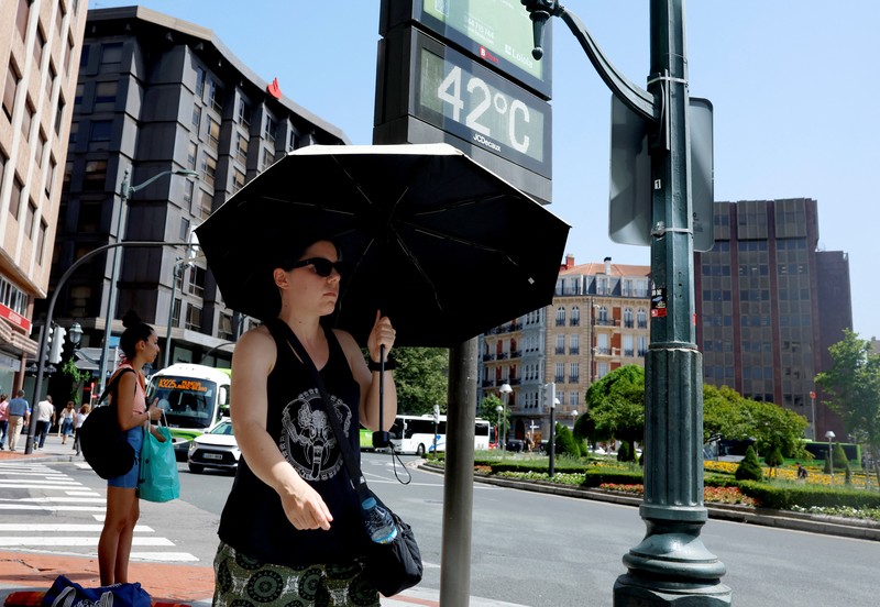 Seorang wanita dengan payung berjalan melewati panel suhu yang menunjukkan angka 42 derajat Celcius selama gelombang panas musim semi di Bilbao, Spanyol, 27 Mei 2026. (REUTERS/Vincent West)