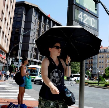 Seorang wanita dengan payung berjalan melewati panel suhu yang menunjukkan angka 42 derajat Celcius selama gelombang panas musim semi di Bilbao, Spanyol, 27 Mei 2026. (REUTERS/Vincent West)