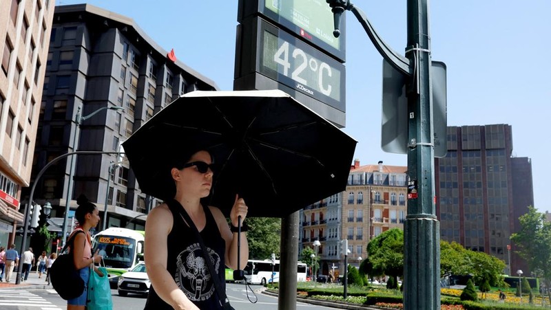 Seorang wanita dengan payung berjalan melewati panel suhu yang menunjukkan angka 42 derajat Celcius selama gelombang panas musim semi di Bilbao, Spanyol, 27 Mei 2026.