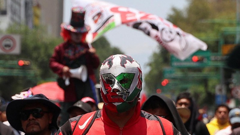 Seorang pria mengenakan topeng pegulat Meksiko saat para guru dari serikat Koordinasi Nasional Pekerja Pendidikan Meksiko (CNTE) berbaris menuju alun-alun Zocalo untuk menuntut upah dan pensiun yang lebih baik, dengan slogan