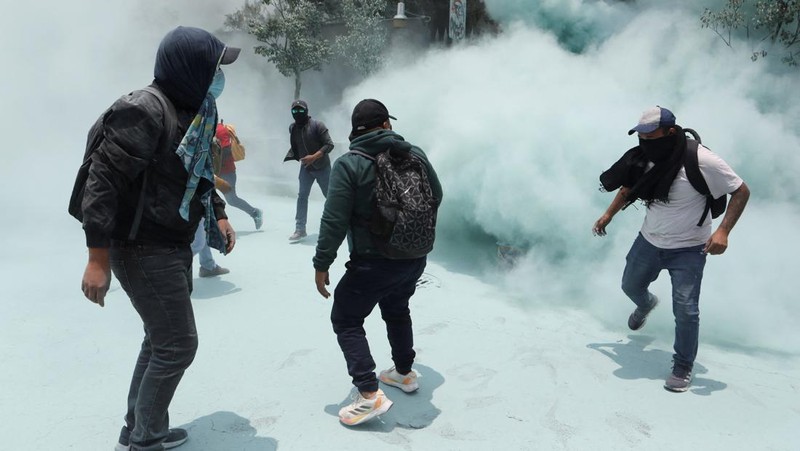Para guru pembangkang dari Koordinasi Nasional Pekerja Pendidikan Meksiko (CNTE) berjalan di tengah asap alat pemadam kebakaran yang digunakan polisi untuk membubarkan demonstran di luar Sekretariat Pendidikan Publik (SEP) selama protes untuk menuntut upah dan pensiun yang lebih baik, dengan slogan