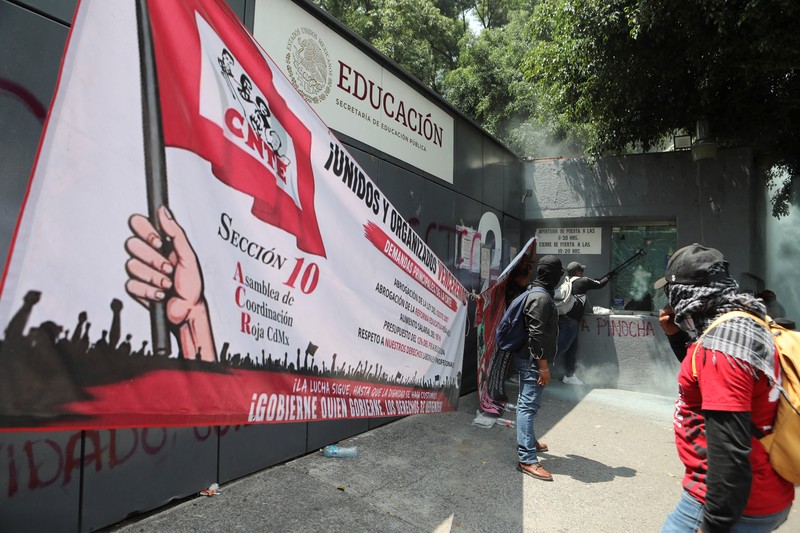 Para guru pembangkang dari Koordinasi Nasional Pekerja Pendidikan Meksiko (CNTE) berkumpul di luar salah satu titik akses ke kantor Sekretariat Pendidikan Publik (SEP) selama protes untuk menuntut upah dan pensiun yang lebih baik, dengan slogan