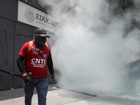 Seorang guru pembangkang dari Koordinasi Nasional Pekerja Pendidikan Meksiko (CNTE) berdiri di tengah gas air mata di luar kantor Sekretariat Pendidikan Publik (SEP) selama protes untuk menuntut upah dan pensiun yang lebih baik, dengan slogan "Jika t