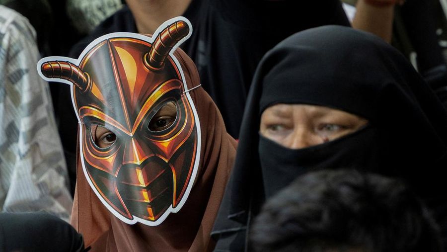 A girl wears a cockroach themed mask, as supporters of the Cockroach Janta Party (CJP) listens to Abhijeet Dipke, head of the CJP, during a sit-in protest demanding the resignation of Indian Education Minister Dharmendra Pradhan, in New Delhi, India,