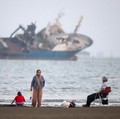 Warga beraktivitas di pesisir Bandar Abbas, Iran, sementara sebuah kapal terlihat melintas di Selat Hormuz, Sabtu (31/5/2026). Jalur pelayaran strategis ini menjadi salah satu urat nadi perdagangan energi dunia karena dilalui sebagian besar ekspor mi