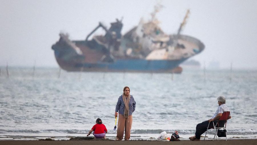Warga beraktivitas di pesisir Bandar Abbas, Iran, sementara sebuah kapal terlihat melintas di Selat Hormuz, Sabtu (31/5/2026). Jalur pelayaran strategis ini menjadi salah satu urat nadi perdagangan energi dunia karena dilalui sebagian besar ekspor mi