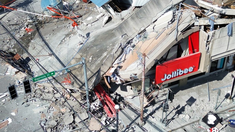 Polisi berkumpul di depan reruntuhan restoran cepat saji Jollibee setelah gempa bumi berkek magnitude 7,8 di Kota General Santos pada 8 Juni 2026. (AFP/EDWIN ESPEJO)