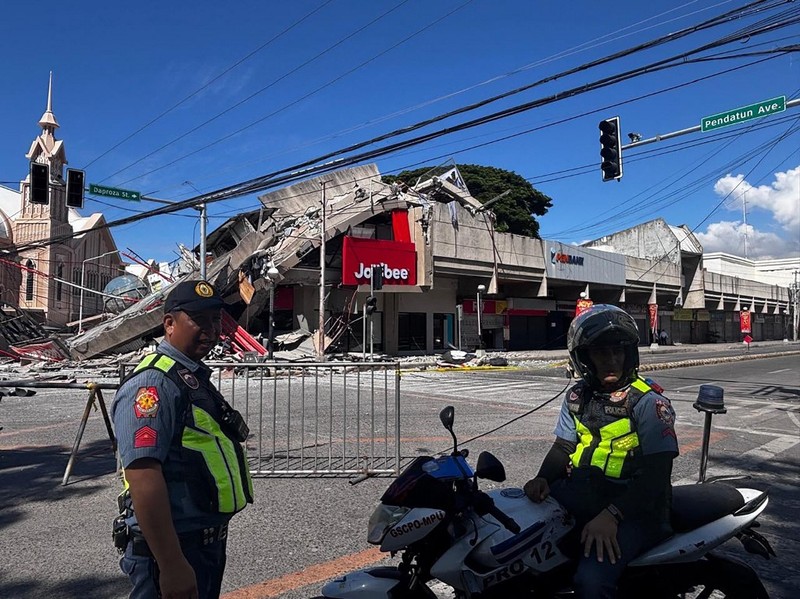 Polisi berkumpul di depan reruntuhan restoran cepat saji Jollibee setelah gempa bumi berkek magnitude 7,8 di Kota General Santos pada 8 Juni 2026. (AFP/EDWIN ESPEJO)