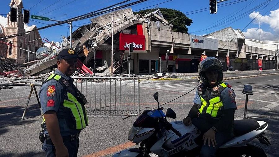 Polisi berkumpul di depan reruntuhan restoran cepat saji Jollibee setelah gempa bumi berkek magnitude 7,8 di Kota General Santos pada 8 Juni 2026. (AFP/EDWIN ESPEJO)
