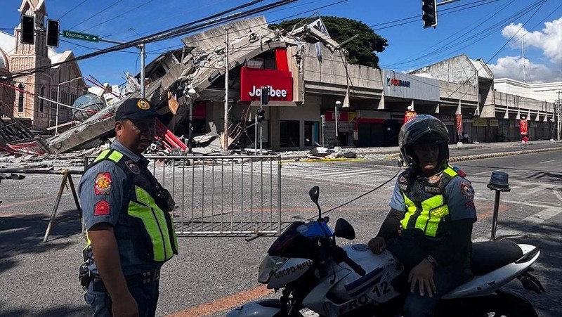 Polisi berkumpul di depan reruntuhan restoran cepat saji Jollibee setelah gempa bumi berkek magnitude 7,8 di Kota General Santos pada 8 Juni 2026. (AFP/EDWIN ESPEJO)