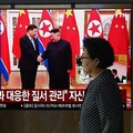 Seorang wanita berjalan melewati layar televisi yang menampilkan siaran berita dengan cuplikan arsip pertemuan tahun 2019 antara Presiden Tiongkok Xi Jinping dan pemimpin Korea Utara Kim Jong Un, di stasiun kereta api di Seoul, Korea Selatan, Senin (