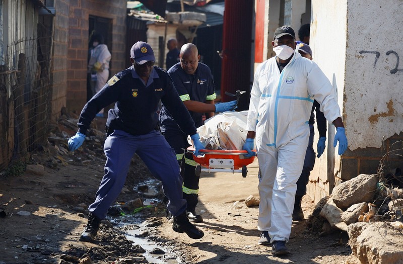 Seorang petugas polisi memberi isyarat di samping anggota tim forensik setelah, menurut polisi, seorang pria bersenjata melepaskan tembakan di permukiman kumuh di Cleveland, Johannesburg, Afrika Selatan, 10 Juni 2026. (REUTERS/Siphiwe Sibeko)