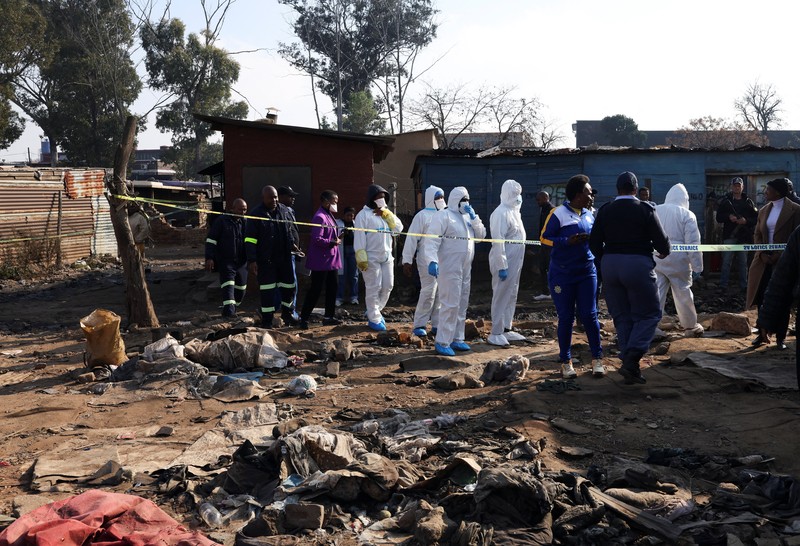 Seorang petugas polisi memberi isyarat di samping anggota tim forensik setelah, menurut polisi, seorang pria bersenjata melepaskan tembakan di permukiman kumuh di Cleveland, Johannesburg, Afrika Selatan, 10 Juni 2026. (REUTERS/Siphiwe Sibeko)