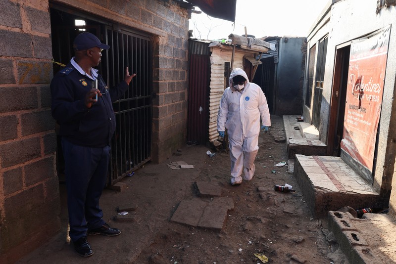 Seorang petugas polisi memberi isyarat di samping anggota tim forensik setelah, menurut polisi, seorang pria bersenjata melepaskan tembakan di permukiman kumuh di Cleveland, Johannesburg, Afrika Selatan, 10 Juni 2026. (REUTERS/Siphiwe Sibeko)