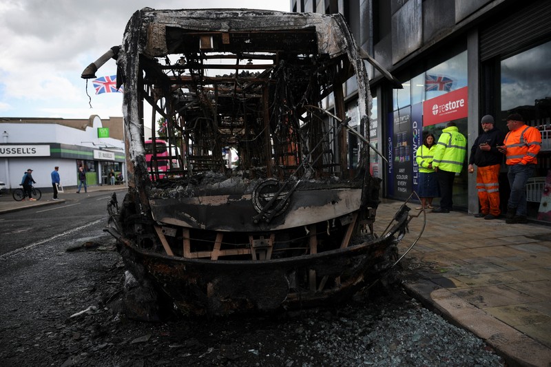 Petugas penegak hukum beroperasi sementara asap mengepul dari kendaraan yang terbakar selama protes setelah serangan pisau pada 8 Juni yang menyebabkan seorang pria terluka parah dan mendorong polisi untuk menyatakan insiden kritis, di Newtownards Road di Belfast, Irlandia Utara, 9 Juni 2026. (REUTERS/Isabel Infantes)