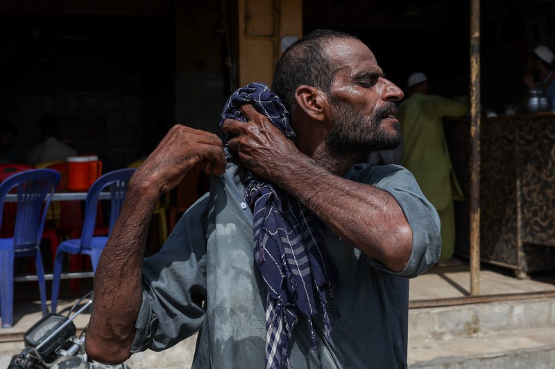 Seorang pengemudi becak motor mendinginkan diri di bawah aliran air sementara seorang pria menyiramkan air ke jalan untuk menurunkan suhu selama hari yang panas di Hyderabad, Pakistan, pada 11 Juni 2026. (REUTERS/Yasir Rajput)