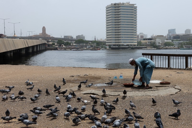Seorang pengemudi becak motor mendinginkan diri di bawah aliran air sementara seorang pria menyiramkan air ke jalan untuk menurunkan suhu selama hari yang panas di Hyderabad, Pakistan, pada 11 Juni 2026. (REUTERS/Yasir Rajput)
