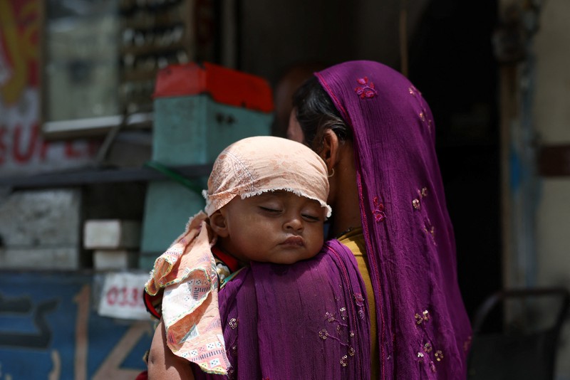 Seorang pengemudi becak motor mendinginkan diri di bawah aliran air sementara seorang pria menyiramkan air ke jalan untuk menurunkan suhu selama hari yang panas di Hyderabad, Pakistan, pada 11 Juni 2026. (REUTERS/Yasir Rajput)