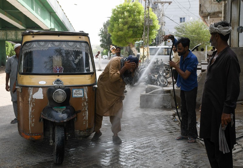 Seorang pengemudi becak motor mendinginkan diri di bawah aliran air sementara seorang pria menyiramkan air ke jalan untuk menurunkan suhu selama hari yang panas di Hyderabad, Pakistan, pada 11 Juni 2026. (REUTERS/Yasir Rajput)