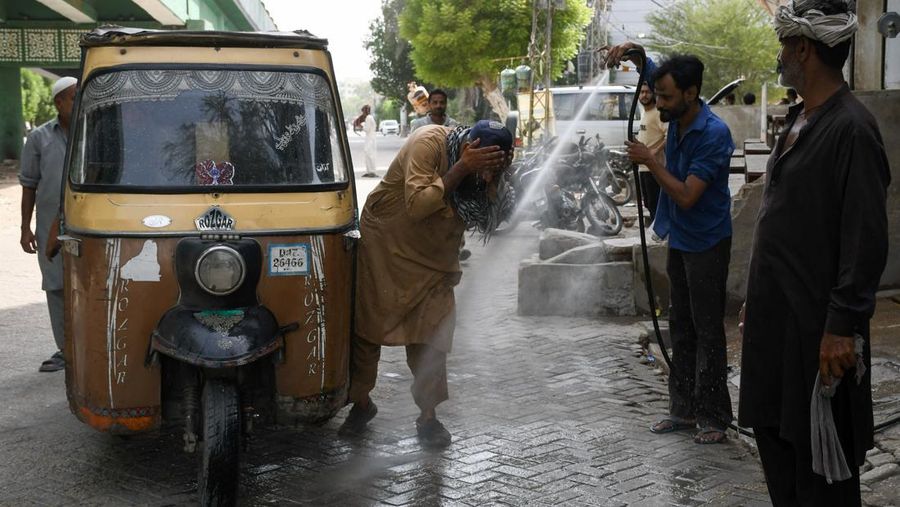Seorang pengemudi becak motor mendinginkan diri di bawah aliran air sementara seorang pria menyiramkan air ke jalan untuk menurunkan suhu selama hari yang panas di Hyderabad, Pakistan, pada 11 Juni 2026. (REUTERS/Yasir Rajput)