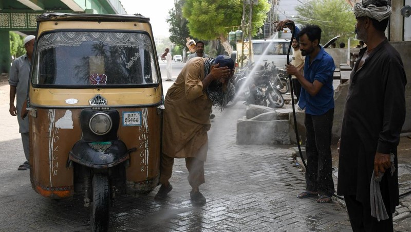 Seorang pengemudi becak motor mendinginkan diri di bawah aliran air sementara seorang pria menyiramkan air ke jalan untuk menurunkan suhu selama hari yang panas di Hyderabad, Pakistan, pada 11 Juni 2026. (REUTERS/Yasir Rajput)