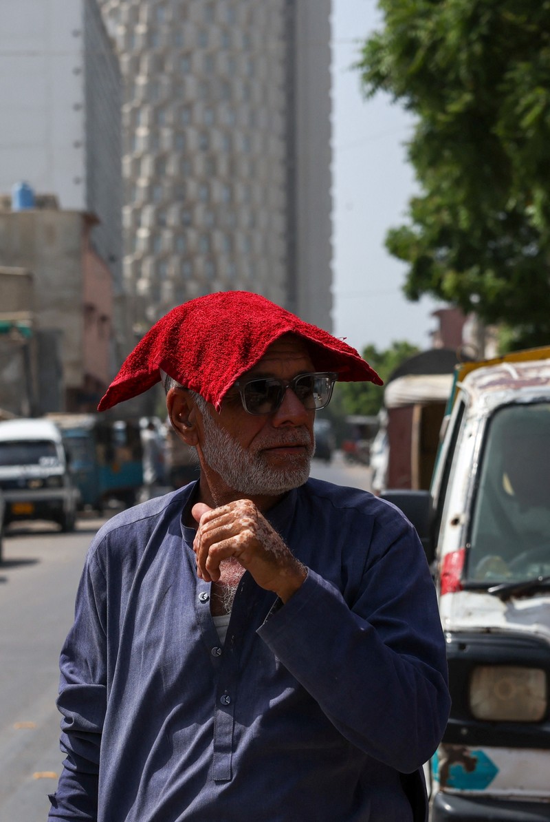 Seorang pengemudi becak motor mendinginkan diri di bawah aliran air sementara seorang pria menyiramkan air ke jalan untuk menurunkan suhu selama hari yang panas di Hyderabad, Pakistan, pada 11 Juni 2026. (REUTERS/Yasir Rajput)