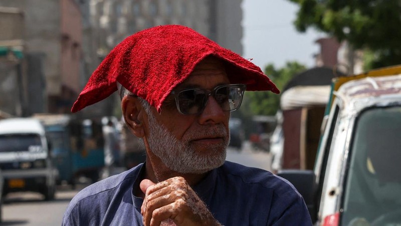 Seorang pria berjalan dengan handuk basah di kepalanya untuk melindungi diri dari terik matahari di hari musim panas yang menyengat di Karachi, Pakistan. 11 Juni 2026.