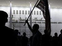 Seorang pria mengangkat bendera nasional AS sementara para pekerja menyiapkan perancah sebelum melepas tulisan dari fasad John F. Kennedy Memorial Center for the Performing Arts, menyusul perintah hakim federal untuk menghapus nama Presiden AS Donald