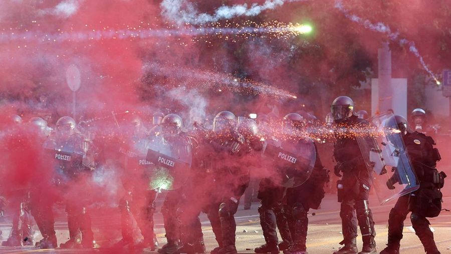 Petugas polisi anti huru hara menggunakan perisai untuk melindungi diri mereka sendiri, sementara kembang api beterbangan di udara, selama bentrokan dengan demonstran, di tengah protes terhadap KTT G7 yang akan datang di Evian-les-Bains di Prancis, di Jenewa, Swiss, 14 Juni 2026.