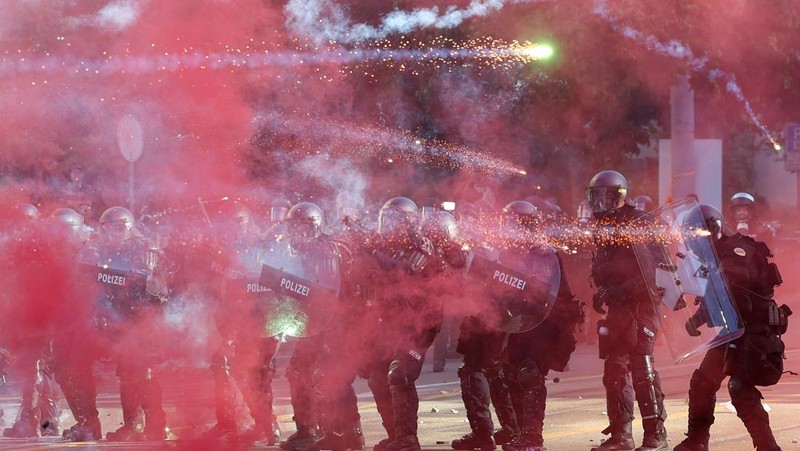 Petugas polisi anti huru hara menggunakan perisai untuk melindungi diri mereka sendiri, sementara kembang api beterbangan di udara, selama bentrokan dengan demonstran, di tengah protes terhadap KTT G7 yang akan datang di Evian-les-Bains di Prancis, di Jenewa, Swiss, 14 Juni 2026.